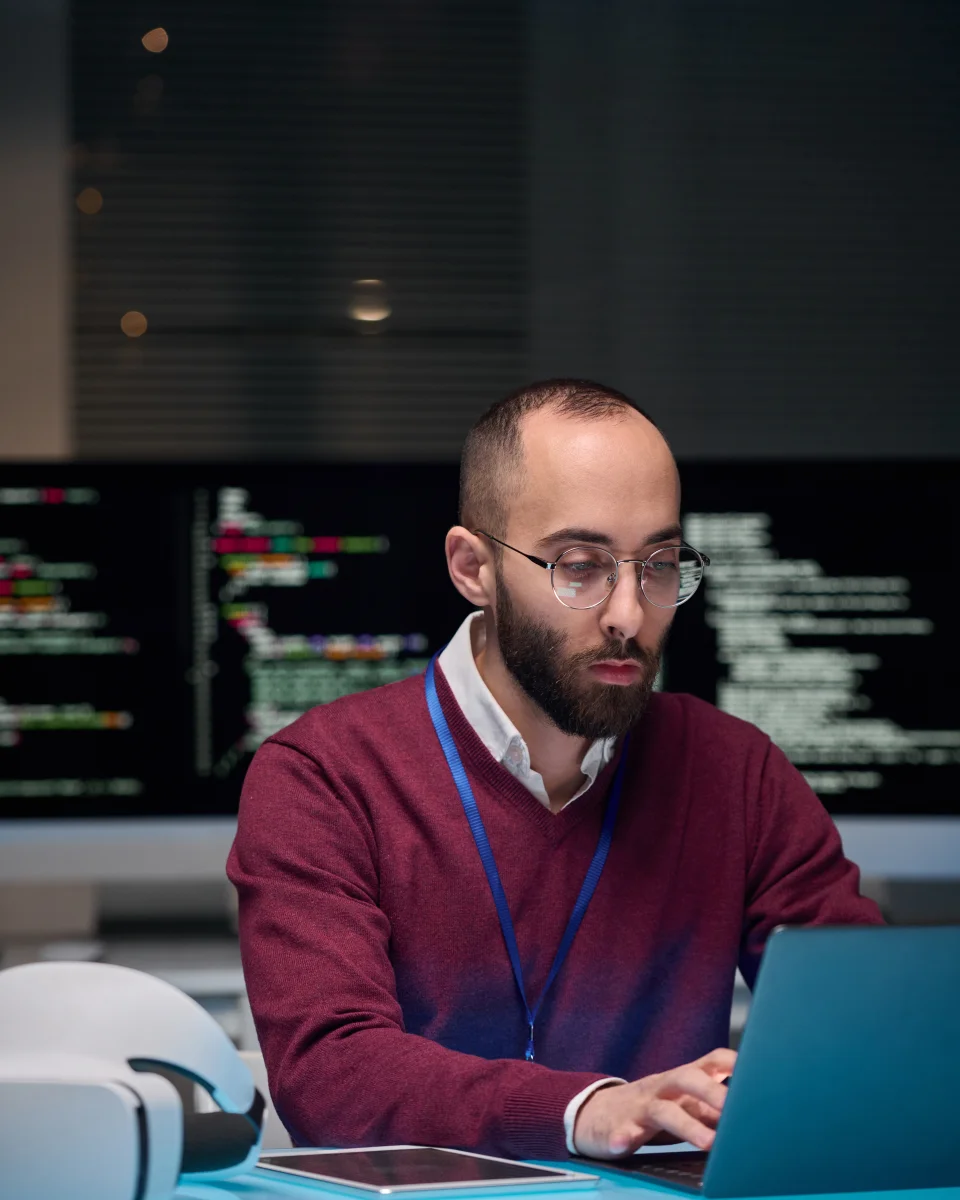 A data engineer working on a laptop in front of code screens
